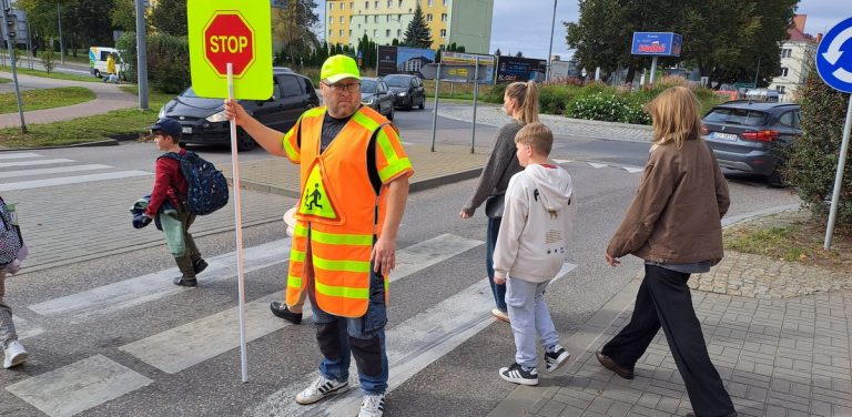 Na zdjęciu przeprowadzacz w jaskrawym oznaczeniu przeprowadza osoby przez przejście