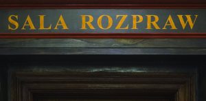 Żółty napis „SALA ROZPRAW” namalowany na ciemnej belce nad zabytkowym, drewnianym portalem drzwiowym. Przed sądem rozpoczął się proces trzech kobiet oskarżonych m.in. o nieudzielenie pomocy i zacieranie śladów po brutalnym zabójstwie 36-latka w Czymanowie, którego ciało ukryto pod wylewką z betonu