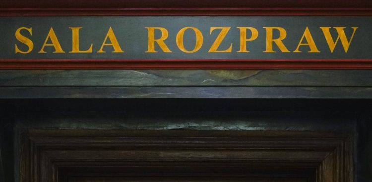 Żółty napis „SALA ROZPRAW” namalowany na ciemnej belce nad zabytkowym, drewnianym portalem drzwiowym. Przed sądem rozpoczął się proces trzech kobiet oskarżonych m.in. o nieudzielenie pomocy i zacieranie śladów po brutalnym zabójstwie 36-latka w Czymanowie, którego ciało ukryto pod wylewką z betonu