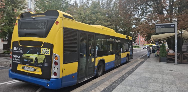 Żółto-niebieski autobus miejski Scania Citywide (MZK Słupsk, numer boczny 3066) stojący na przystanku w centrum miasta. W tle widać elektroniczną tablicę odjazdów, zieleń miejską oraz ogródek kawiarniany. Zarząd Infrastruktury Miejskiej w Słupsku wprowadził nowe bilety, a także zmiany w istniejących. Mają one zachęcać mieszkańców do częstszego korzystania z komunikacji zbiorowej