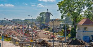 Plac budowy infrastruktury kolejowej i drogowej z widocznymi dźwigami, koparkami i budynkiem nastawni
