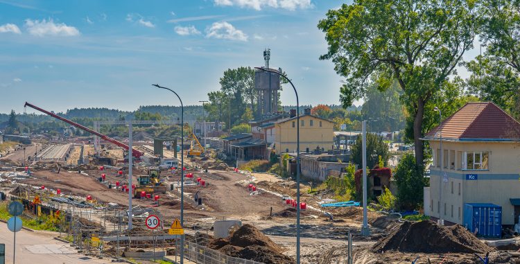 Plac budowy infrastruktury kolejowej i drogowej z widocznymi dźwigami, koparkami i budynkiem nastawni