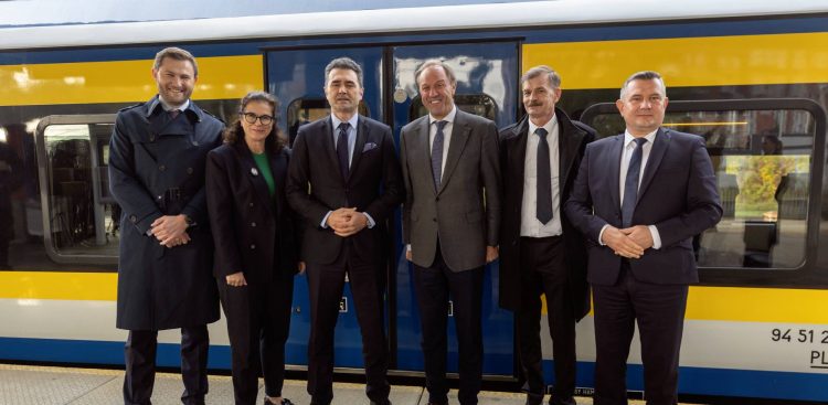 Przedstawiciele rządu i pomorskich samorządów - w tym Piotr Borawski, Aleksandra Dulkiewicz, Piotr Malepszak i Mieczysław Struk – stoją na peronie kolejowym na tle żółto-niebieskiego składu pociągu