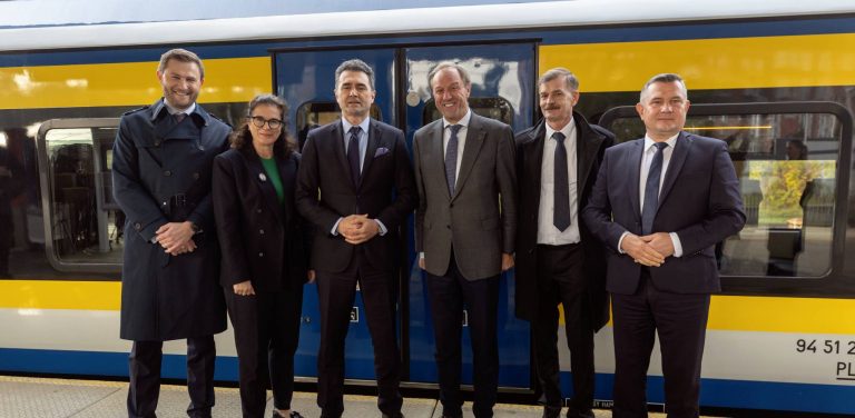 Przedstawiciele rządu i pomorskich samorządów - w tym Piotr Borawski, Aleksandra Dulkiewicz, Piotr Malepszak i Mieczysław Struk – stoją na peronie kolejowym na tle żółto-niebieskiego składu pociągu