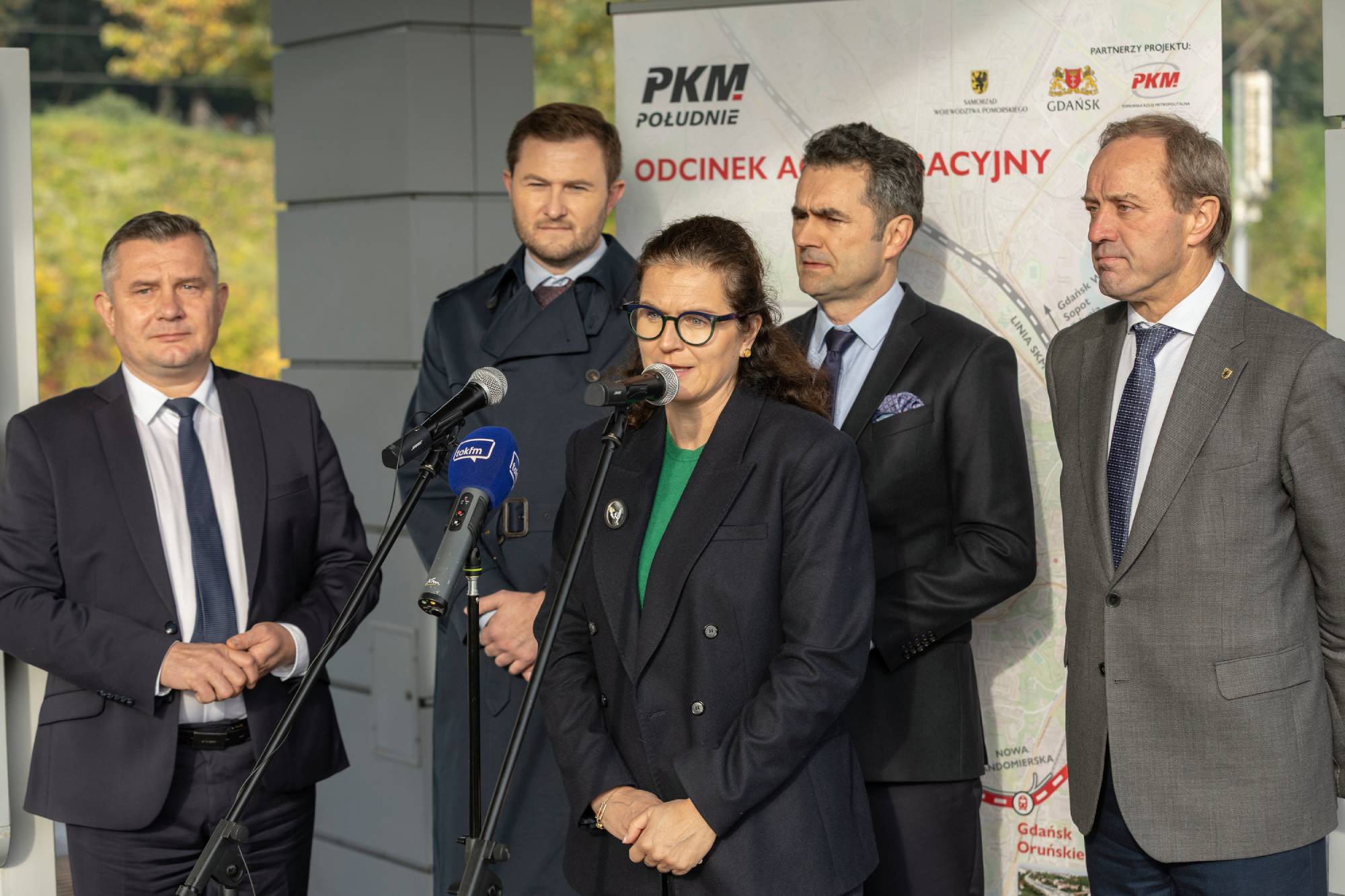 Prezydent Gdańska Aleksandra Dulkiewicz przemawia do mikrofonów podczas briefingu prasowego na tle mapy PKM Południe, obok stoją m.in. Piotr Malepszak i Mieczysław Struk