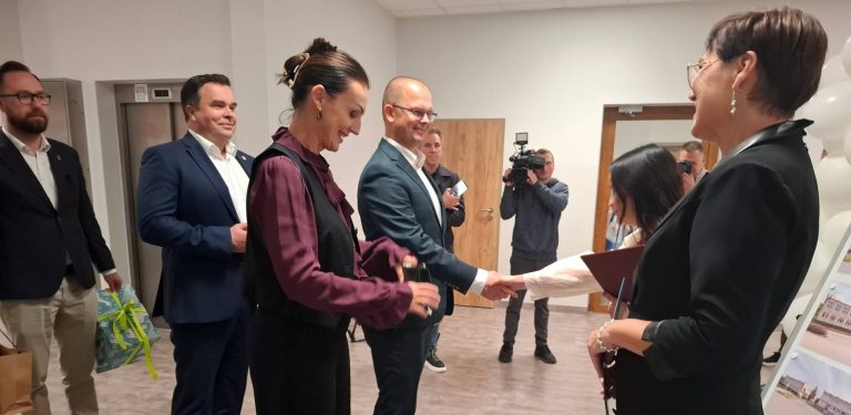 Wojewoda pomorska Beata Rutkiewicz oraz burmistrz Lęborka Jarosław Litwin składają gratulacje dyrekcji podczas oficjalnego otwarcia Publicznego Żłobka nr 1 w Lęborku. W tle widać korytarz placówki i operatora kamery