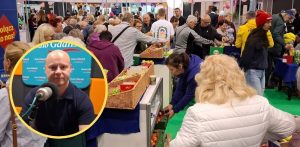 Tłum odwiedzających stoiska wystawiennicze w hali targowej z koszami produktów; w lewym dolnym rogu w okrągłej ramce wklejone zdjęcie Łukasza Iwaszkiewicza przed mikrofonem w studiu Radia Gdańsk